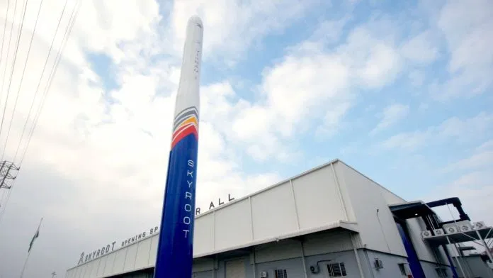 The Vikram-1 rocket standing vertically outside Skyroot Aerospace's manufacturing facility, painted in the company's blue and orange livery with the Skyroot wordmark visible on the fuselage.